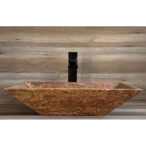 May include: A rectangular, brown, stone vessel sink with a textured surface. The sink is on a wood-grain countertop with a black faucet.