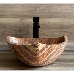 May include: A brown and beige stone vessel sink with a square shape and a wavy, organic design. The sink is shown with a black faucet.
