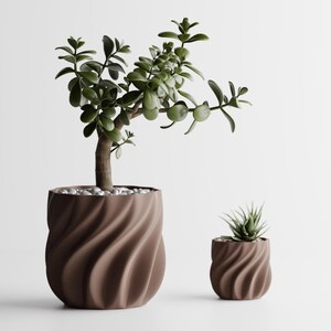 May include: Two brown planters with a vertical spiral texture. The larger planter holds a jade plant with thick green leaves, while the smaller planter contains a small succulent. Both pots are filled with small white decorative stones.