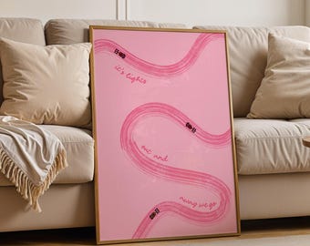 May include: A framed pink art print with a gold frame. The print features a winding, abstract design in shades of pink, with the words "it's lighter" and "out and moving we go" in white script. The artwork is displayed in a living room setting.