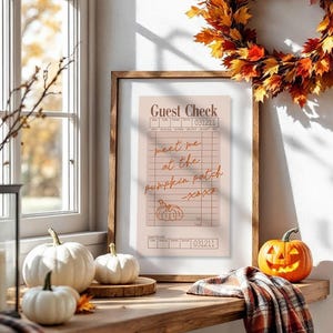 May include: A fall-themed vignette featuring a framed "Guest Check" print with handwritten text, a pumpkin-shaped jack-o'-lantern, and a decorative leaf wreath. White pumpkins and a plaid scarf add to the autumn ambiance. The scene is set on a wooden shelf.