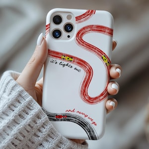 May include: White phone case with a red and black race track design. The case features the text "it's lights out" and "and away we go". The design includes yellow and red race cars.