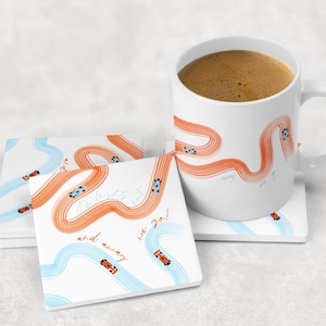 Könnte beinhalten: Weißer Keramikbecher und Untersetzer mit Rennwagen-Motiv. Der Becher und die Untersetzer zeigen orangefarbene und blaue Rennstrecken mit kleinen Rennwagen. Auf den Untersetzern steht der Text "the lights out and away we go!"
