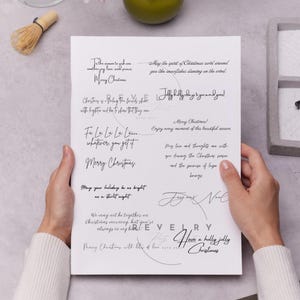 May include: A white sheet of paper with handwritten Christmas greetings in black script. The paper is held by a person, with a neutral background featuring a matcha whisk and a zen garden.