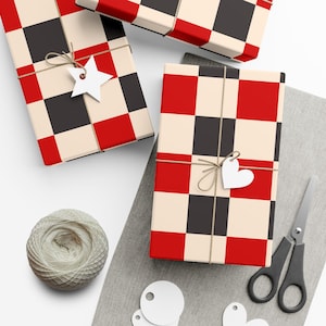 Peut inclure: Trois cadeaux rectangulaires emballés dans du papier à motif à carreaux rouge, noir et crème. Chaque paquet est noué avec de la ficelle fine et comporte une étiquette en papier blanc en forme d'étoile ou de cœur. Une pelote et des ciseaux.