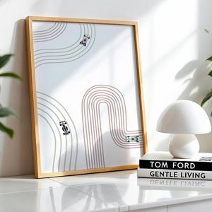 Puede incluir: Una impresión enmarcada con un diseño minimalista de coche de carreras y un marco de madera clara. La obra de arte representa una pista con coches de carreras en tonos grises y marrones. Una lámpara de seta blanca y libros están en primer plano.
