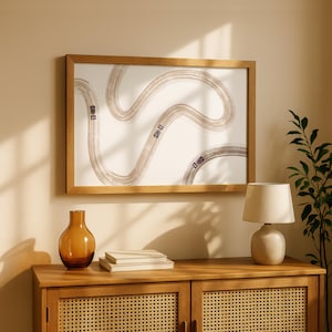 Op de afbeelding: Een ingelijste print met een kronkelende racebaan met drie kleine paarse raceauto's. De print zit in een licht houten frame en hangt boven een houten kast met een lamp, boeken en een decoratieve vaas.