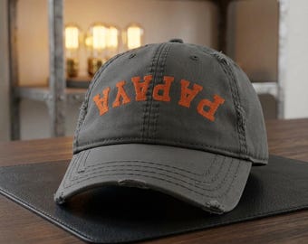 May include: A gray, distressed baseball cap with the word "PAPAYA" in orange block letters across the front. The cap has a curved brim and a worn appearance, suggesting a vintage or casual style.
