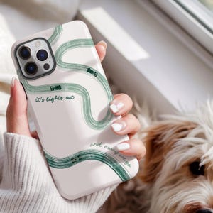 May include: White phone case with a green abstract design of a race track and the text "it's lights out and away we go". The case has a glossy finish and a camera cutout.