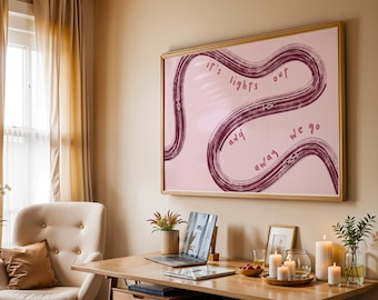 May include: A framed artwork with the text "it's lights out and away we go" in a cursive font. The artwork is in a room with a desk, laptop, candles, and a beige armchair. The artwork has a pink background with a dark red wavy design.