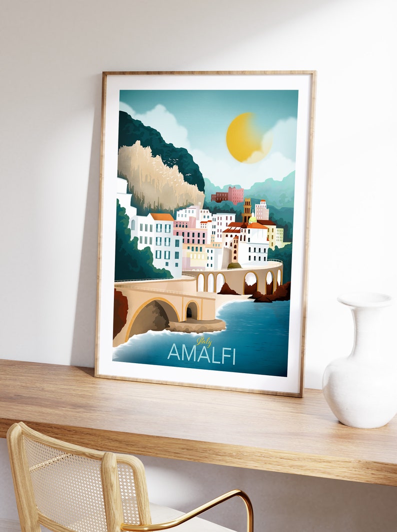 May include: A framed art print featuring a stylized illustration of Amalfi, Italy. The artwork depicts a coastal town with colorful buildings, a bridge, and the text "Italy Amalfi". The color palette includes blues, yellows, and whites.