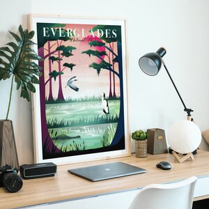 May include: A framed art print featuring a colorful illustration of the Everglades National Park. The artwork depicts a swamp scene with birds, trees, and the text "EVERGLADES National Park" at the top. The print is displayed on a wooden desk.