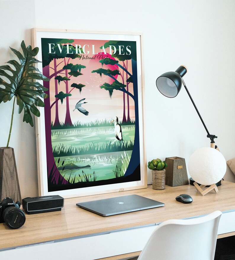 May include: A framed art print featuring a colorful illustration of the Everglades National Park. The artwork depicts a swamp scene with birds, trees, and the text "EVERGLADES National Park" at the top. The print is displayed on a wooden desk.
