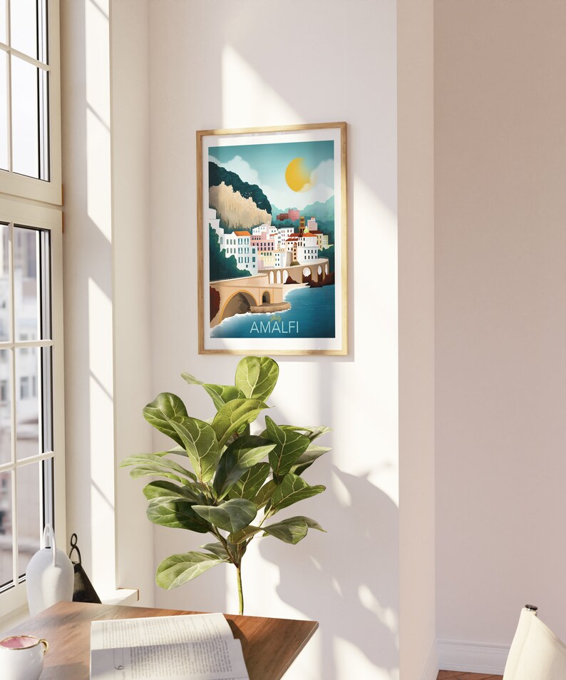 May include: A framed art print featuring a colorful illustration of Amalfi, Italy. The artwork depicts a coastal town with white buildings, a bridge, and a bright yellow sun. The word "AMALFI" is printed at the bottom of the image.