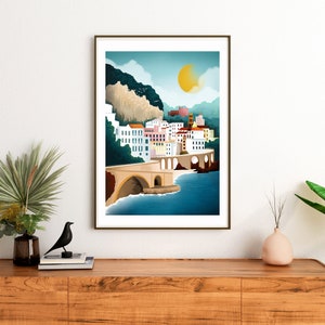 May include: A framed art print depicting a coastal town scene. The artwork features a bridge, buildings with colorful facades, and a large yellow sun in a blue sky. The print is displayed on a wooden cabinet with decorative items.