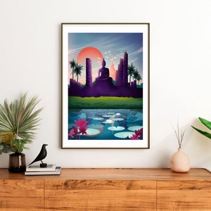 May include: Framed art print showing a tranquil scene with a seated Buddha, temples, and palm trees set against a sunset. A reflective body of water with lily pads and lotus flowers is in the foreground. The artwork is displayed on a wooden cabinet.