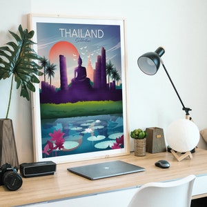 May include: A framed art print of a Thailand Sukhothai landscape. The artwork shows a seated Buddha, temples, and palm trees under a sunset. The print is on a wooden desk with a laptop, lamp, and decorative items.