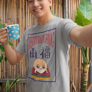 May include: A gray t-shirt with a graphic of a cartoon desert rain frog on a red and yellow watermelon slice. The text "DESERT RAIN FROG" and "雨福" are printed on the graphic.