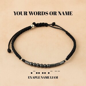 Puede incluir: Pulsera de cuerda negra con cuentas cuadradas negras y detalles plateados. "YOUR WORDS OR NAME" está escrito encima de la pulsera. "EXAPLE NAME LIAM" está escrito debajo de la pulsera.