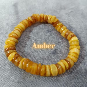 May include: A bracelet made of amber beads. The beads are a warm, honey color and are arranged in a circular pattern. The bracelet is labeled "Amber".