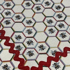May include: White fabric with a red scalloped border. The fabric has a repeating pattern of bees in hexagonal cells.