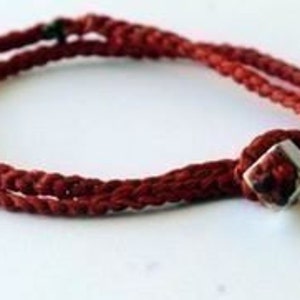 May include: A red braided cord bracelet with a silver square bead.