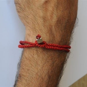 May include: A red braided bracelet with a silver charm. The bracelet is worn on a person's wrist.