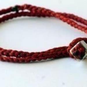 May include: A red braided cord bracelet with a silver square bead.