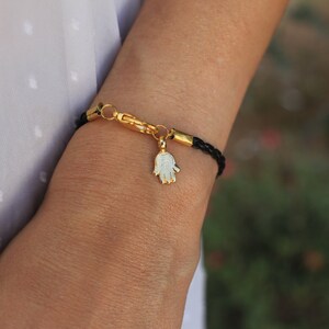 May include: A black leather bracelet with a gold clasp and a gold hamsa charm.