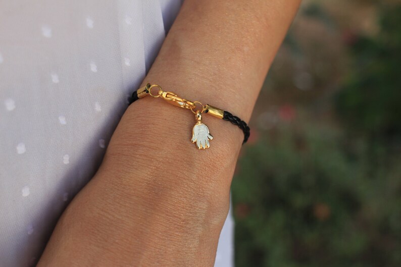 May include: A black leather bracelet with a gold clasp and a gold hamsa charm.
