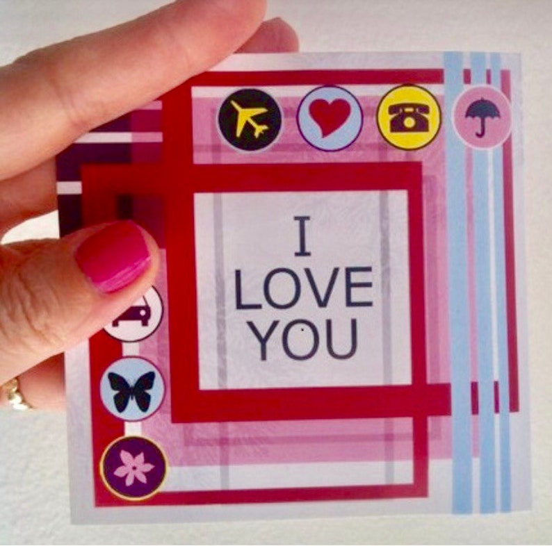 May include: Red and white card with a pink and blue plaid pattern. The card says "I love you" in a white box. There are small icons around the border of the card, including a plane, a heart, a phone, an umbrella, a car, a butterfly, and a flower.