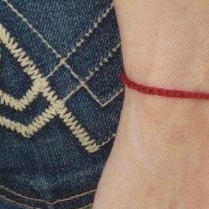 May include: A red string bracelet with a silver charm. The bracelet is worn on a person's wrist.
