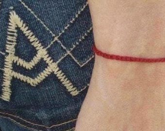 Könnte beinhalten: Ein rotes Armband mit einem silbernen Anhänger. Das Armband wird am Handgelenk getragen.