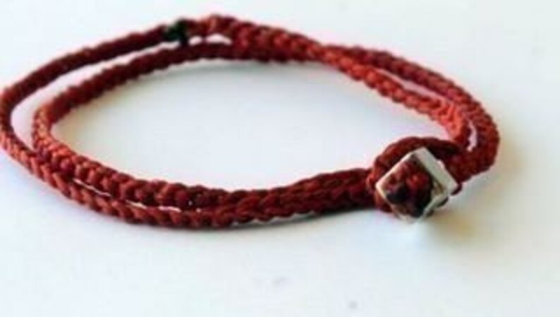 May include: A red braided cord bracelet with a silver square bead.