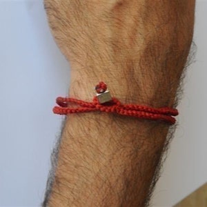 May include: A red braided bracelet with a silver square charm.