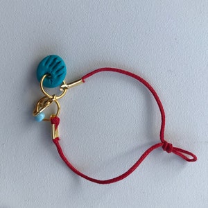 May include: A red string bracelet with a gold charm featuring a blue circle with a design.