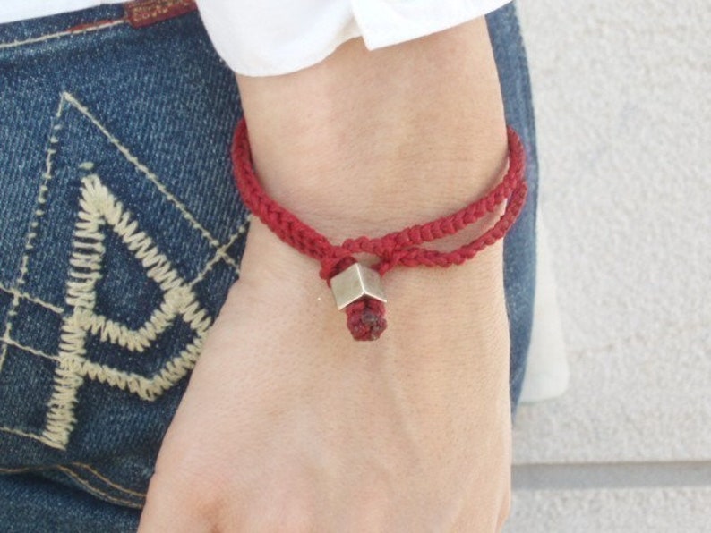 May include: A red braided bracelet with a silver cube charm.