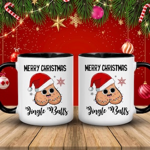 May include: Two white ceramic mugs with black handles and rims. Each mug features the text "MERRY CHRISTMAS" above a cartoon design of testicles wearing a Santa hat and Christmas lights. The text "Jingle Balls" is below the design.