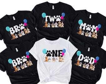 May include: Black and white t-shirts with dog-themed birthday designs. The shirts feature the words "BR", "TWO", "MOM", "DAD", and "ONE" with paw prints and balloon graphics. A variety of dog breeds are depicted.