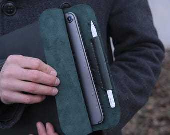 May include: A dark green leather case with a flap that opens to reveal a tablet and a stylus. The case has a pocket for the stylus.