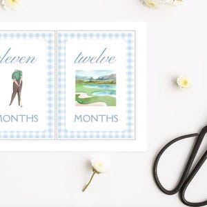 May include: Two printable cards with a blue and white gingham pattern. The first card says "eleven months" and features a golfer. The second card says "twelve months" and features a watercolour illustration of a golf course.