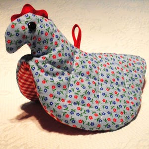 May include: A handmade chicken-shaped oven mitt. The mitt is primarily light blue with a floral pattern of red and blue flowers. The comb is red, and the wattle is red and white checkered. A red loop is attached for hanging.