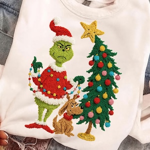 May include: White sweatshirt featuring an embroidered Grinch character in a Santa hat and red coat, holding Christmas lights. A decorated Christmas tree and a brown dog are also embroidered on the front. Festive holiday apparel.