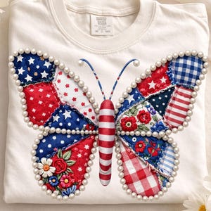 May include: A white sweatshirt with a patriotic butterfly design. The butterfly wings are made of red, white, and blue patchwork, edged with pearls. The butterfly's body is red and white striped, with blue antennae.