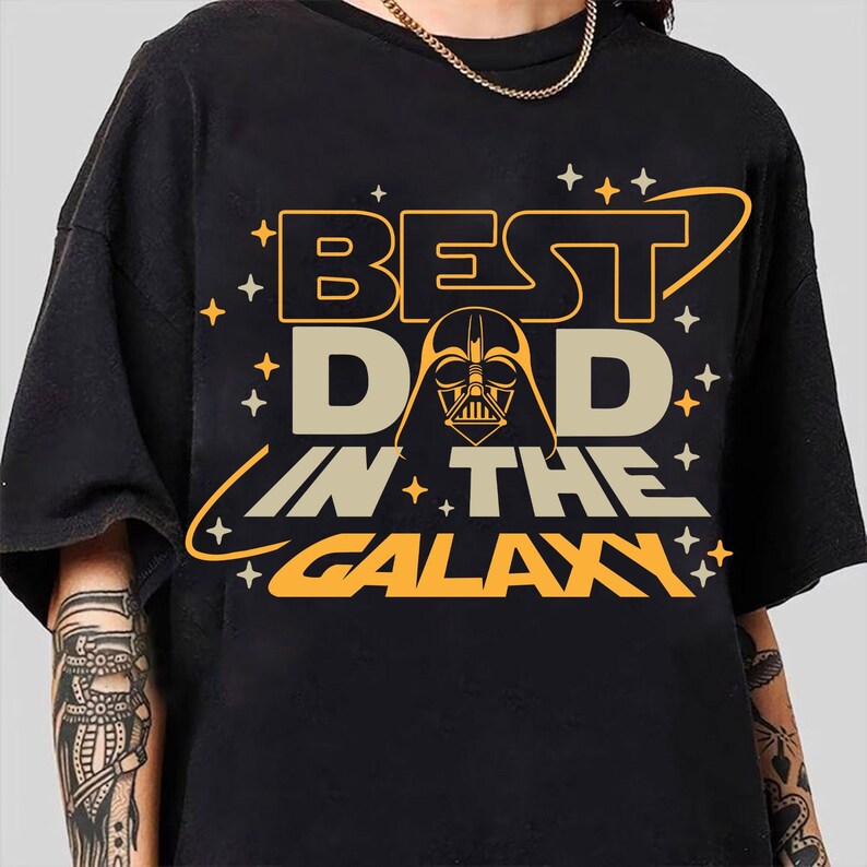May include: Black t-shirt with a yellow and orange graphic that says "Best Dad in the Galaxy" with a Darth Vader silhouette.