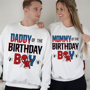 May include: White sweatshirts with red and blue text that says "Daddy of the Birthday Boy" and "Mommy of the Birthday Boy".  The text is surrounded by a spider web design with a cartoon Spiderman in the center.