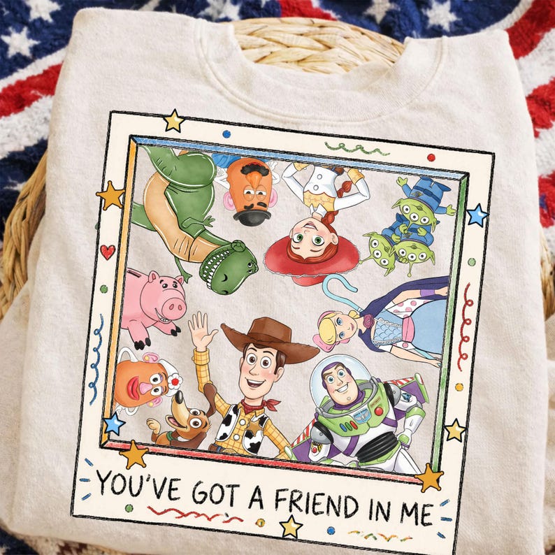 Puede incluir: Sudadera beige con un gr&aacute;fico enmarcado de personajes de la pel&iacute;cula animada "Toy Story". La imagen incluye a Woody, Buzz Lightyear, Rex y otros personajes. El texto "YOU'VE GOT A FRIEND IN ME" est&aacute; en la parte inferior del marco.