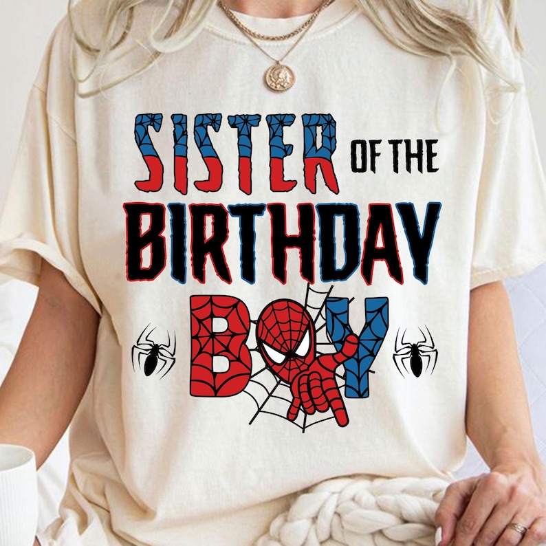 May include: White t-shirt with the text "Sister of the Birthday Boy" in black. A red and blue Spiderman character is in the center of the shirt with a web design.