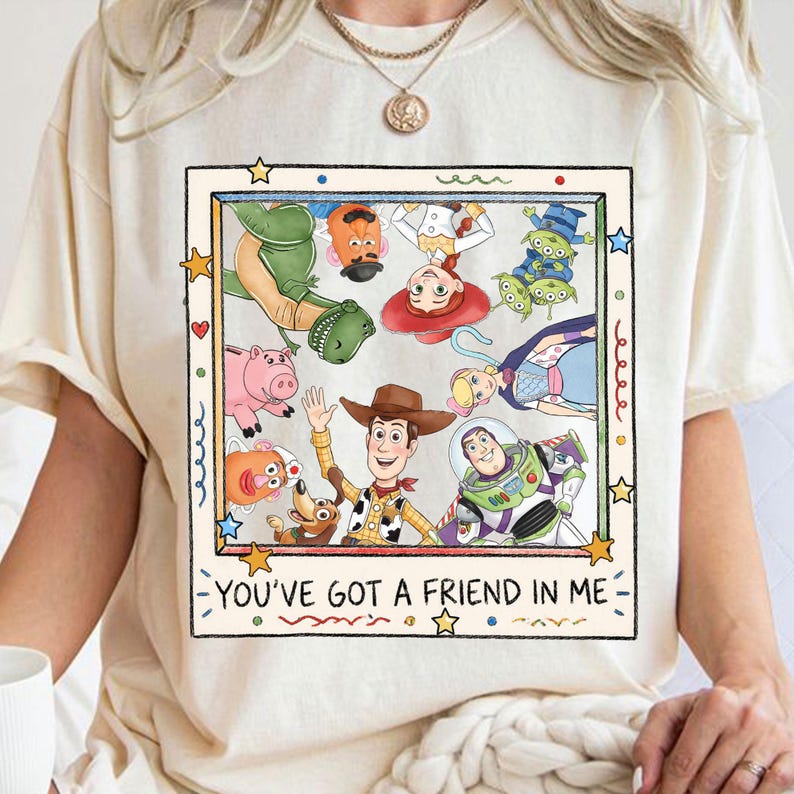 Puede incluir: Camiseta color crema con un dise&ntilde;o gr&aacute;fico colorido de personajes de Toy Story, incluyendo a Woody y Buzz Lightyear. El dise&ntilde;o est&aacute; enmarcado e incluye el texto "YOU'VE GOT A FRIEND IN ME".
