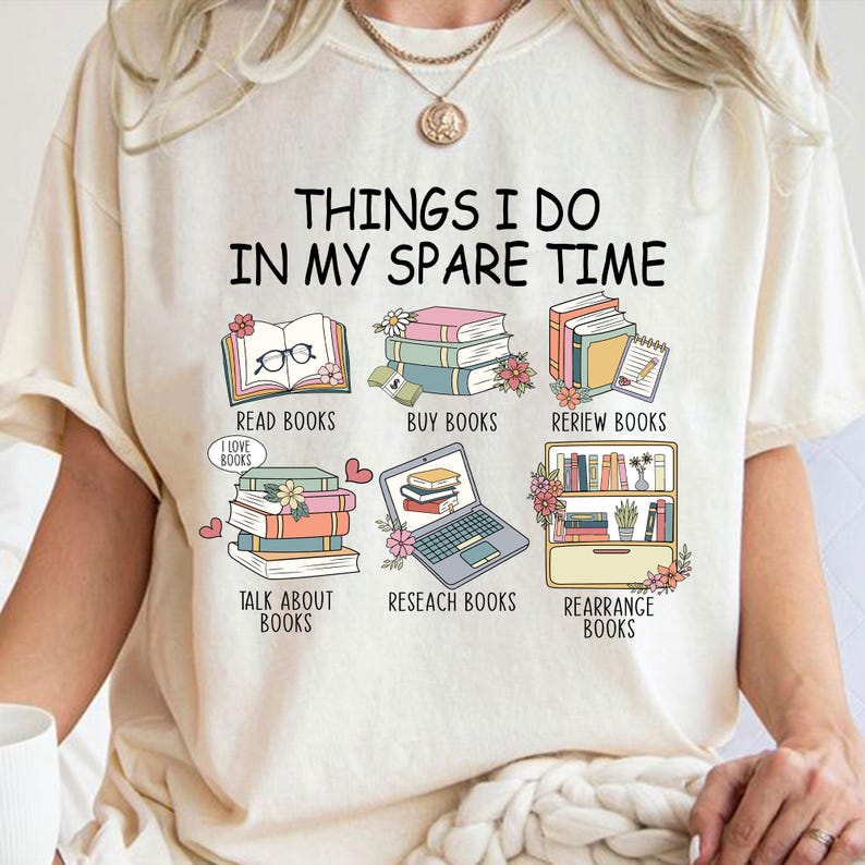 May include: A white t-shirt with the text "Things I do in my spare time" and illustrations of books, a laptop, and a bookshelf. The illustrations are in a cartoon style and feature a variety of colors.